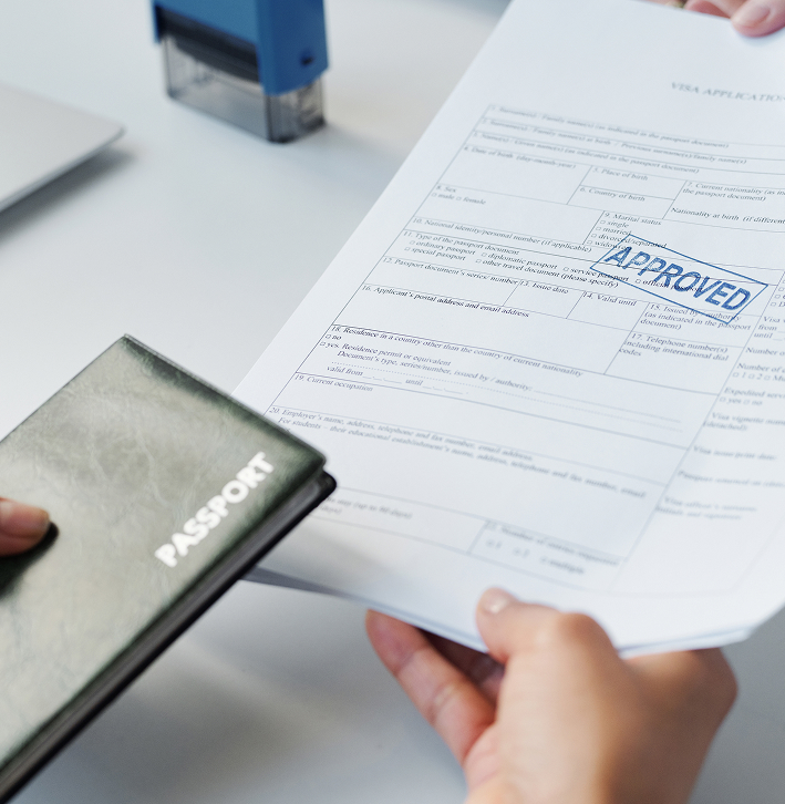 A person holds a passport and hands over a Canada visa application form with an APPROVED stamp, highlighting success in migration law.