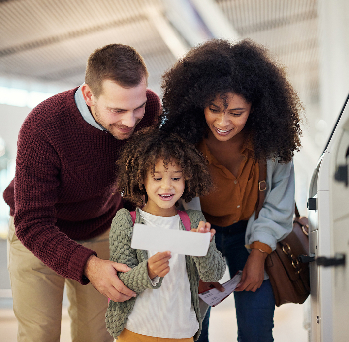 A family of three, two adults and a child, look at a boarding pass together at an airport self-service kiosk in Canada, preparing for their next step in the immigration process.